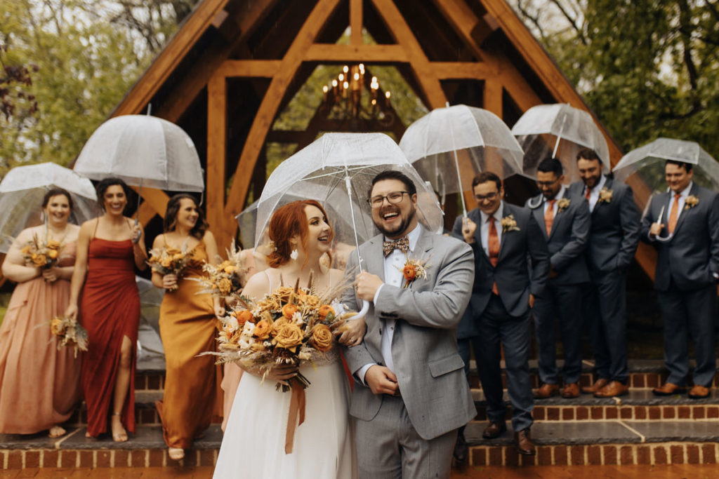 wedding party posing with umbrellas in the rain