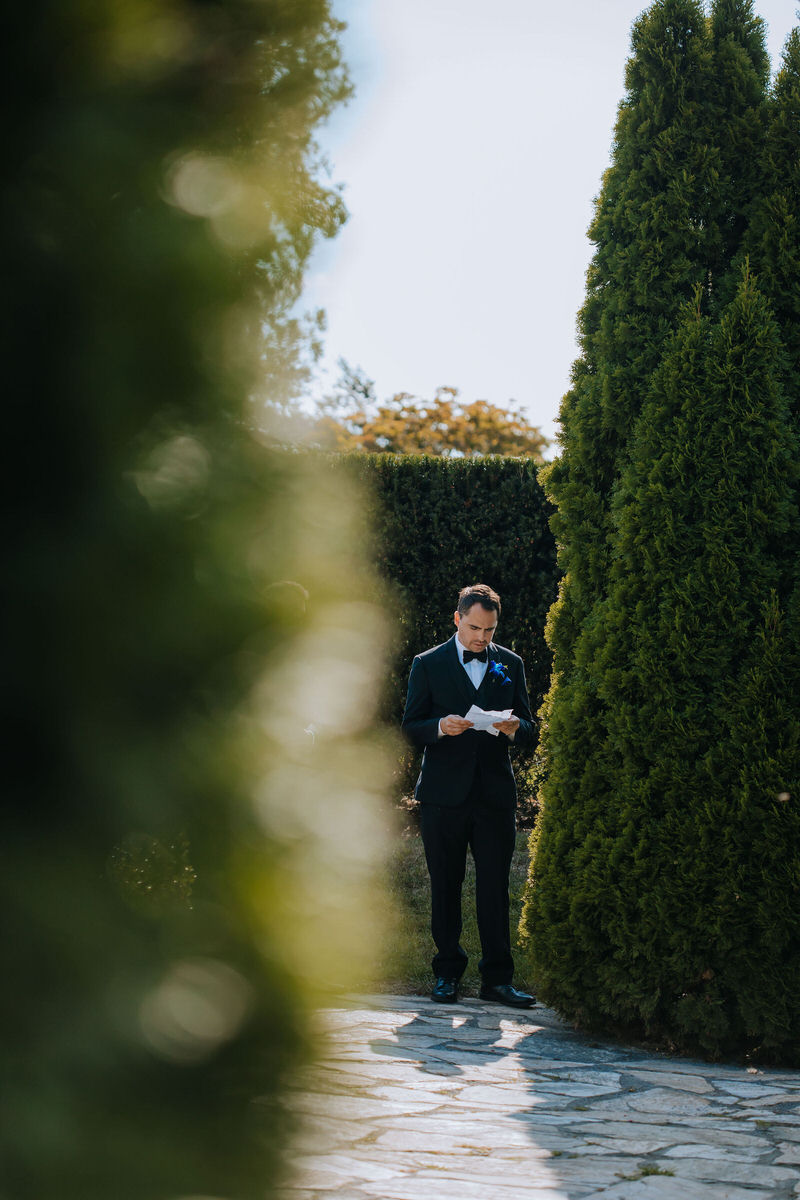Celebrant reading a note in between large shrubs 