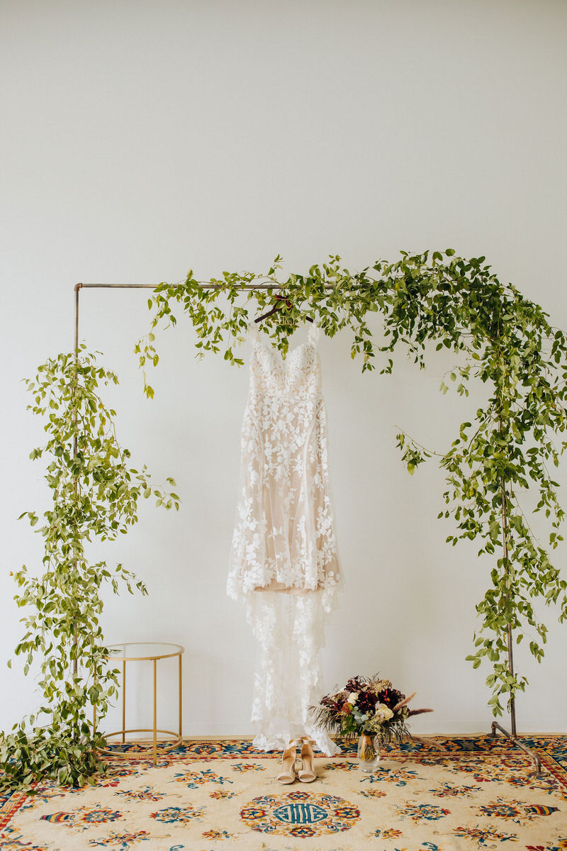 wedding dress hanging from metal pole covered in vines
