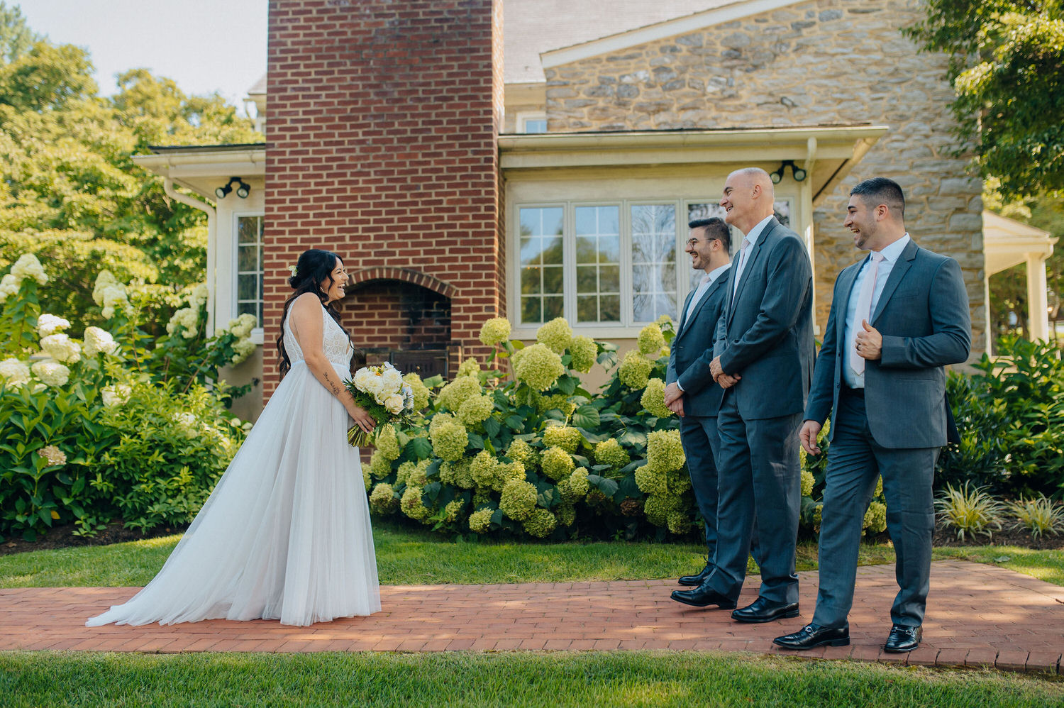 Celebrant in a white dress looking at group of people in tuxedoes during a first look.