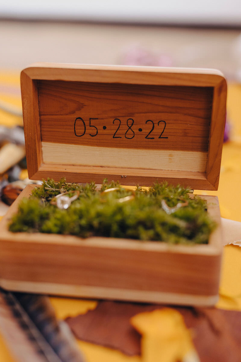 open wooden box with green moss and rings inside with 05 28 22 written on the inside