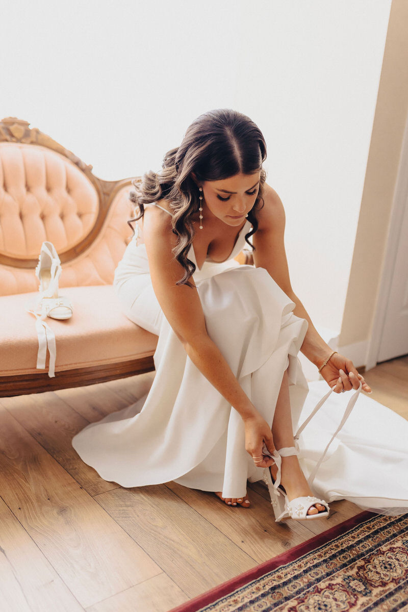 person in their wedding dress sitting on a small couch putting on shoes