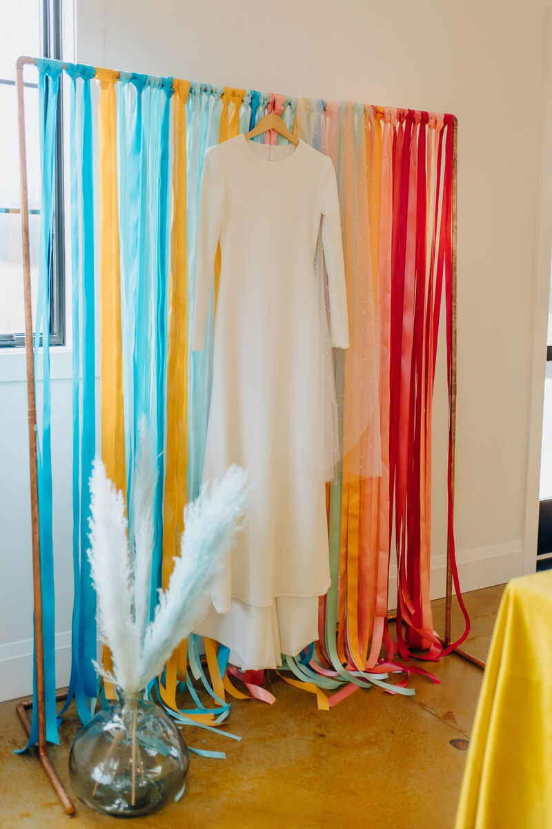 wedding dress hanging up with colorful streamers behind it