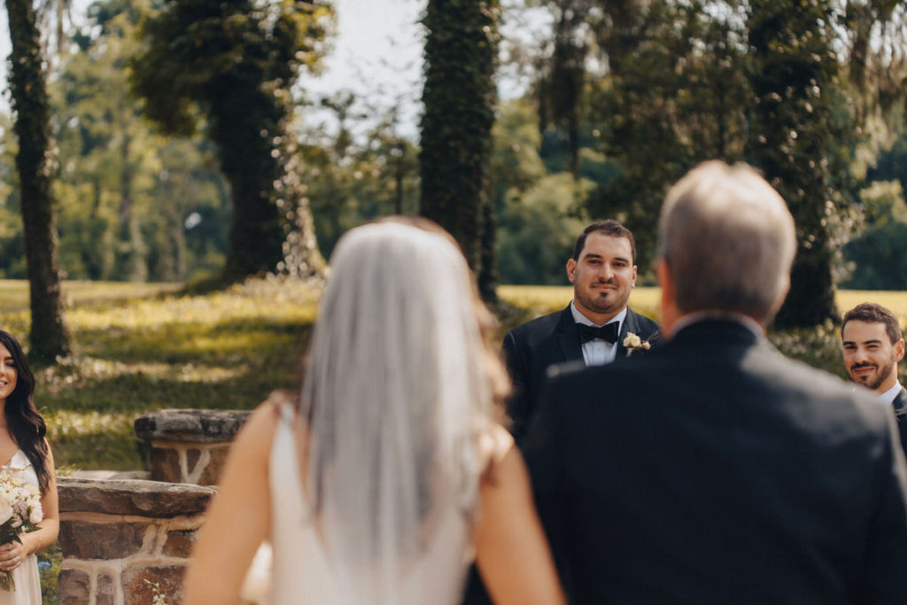 celebrant walking down the aisle with their father while partner waits at the end