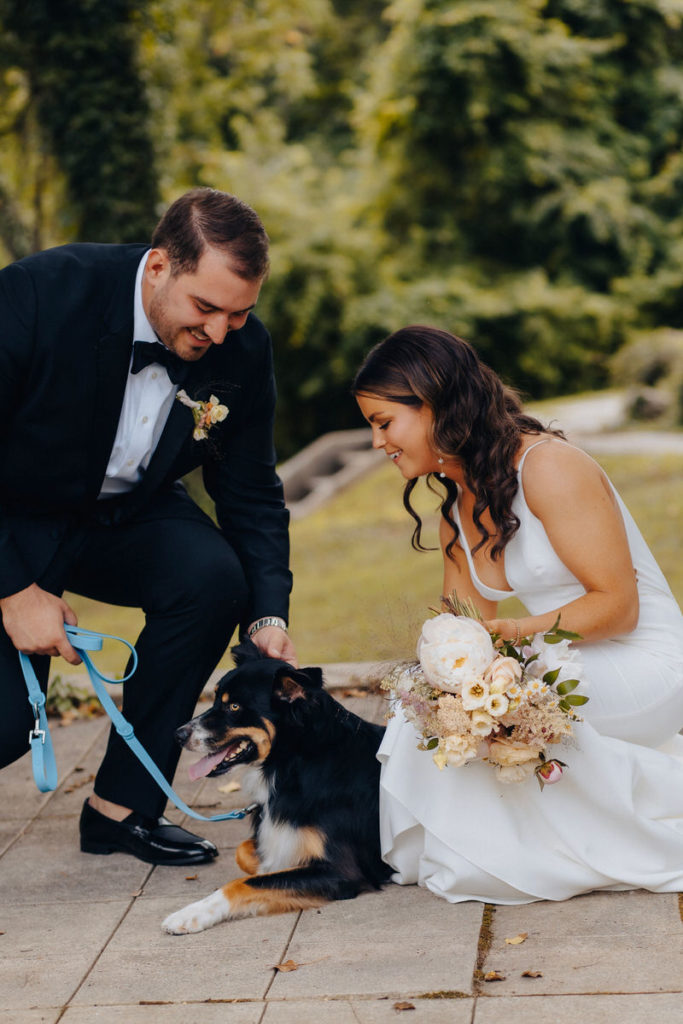couple leaning down and smiling while petting their dog 