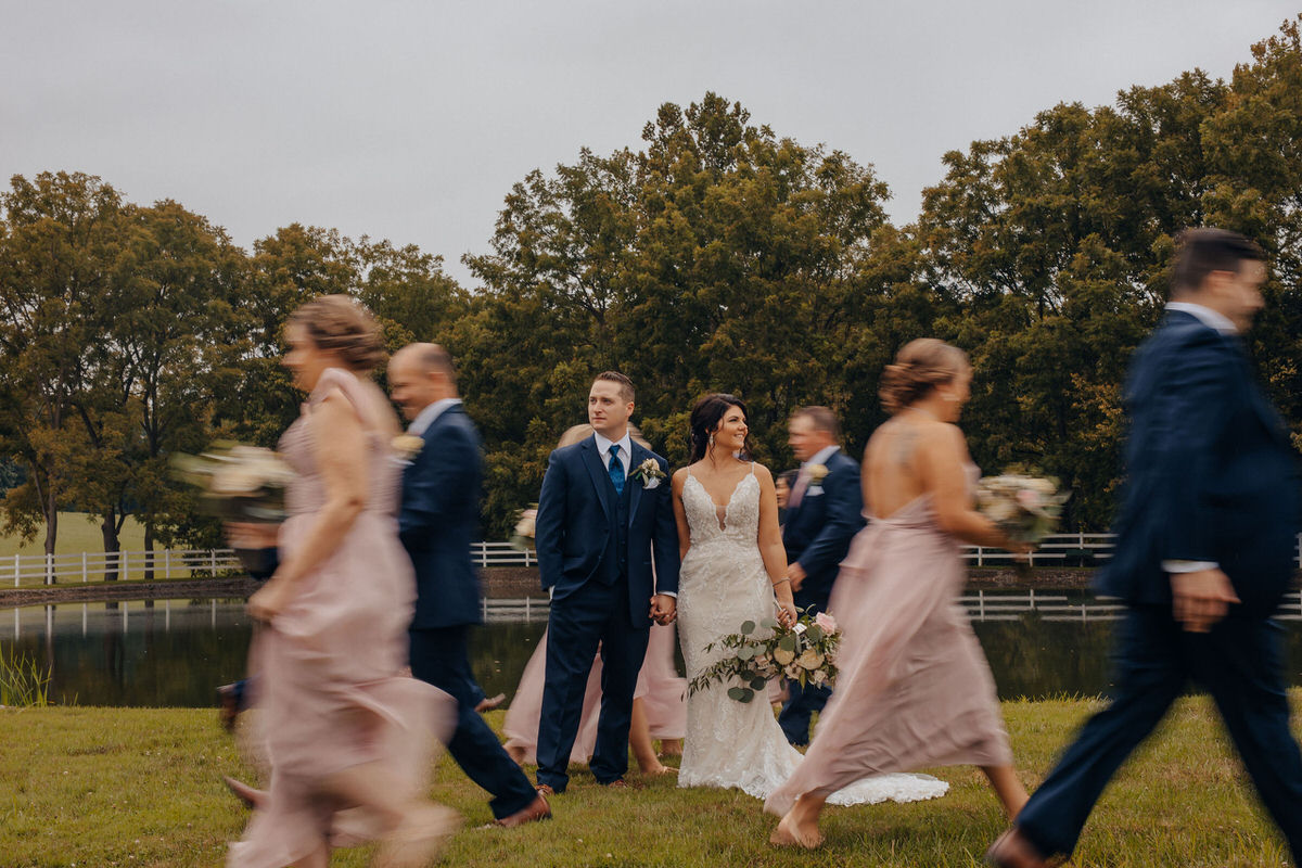 couple standing together with their bridal party walking around them blurred out