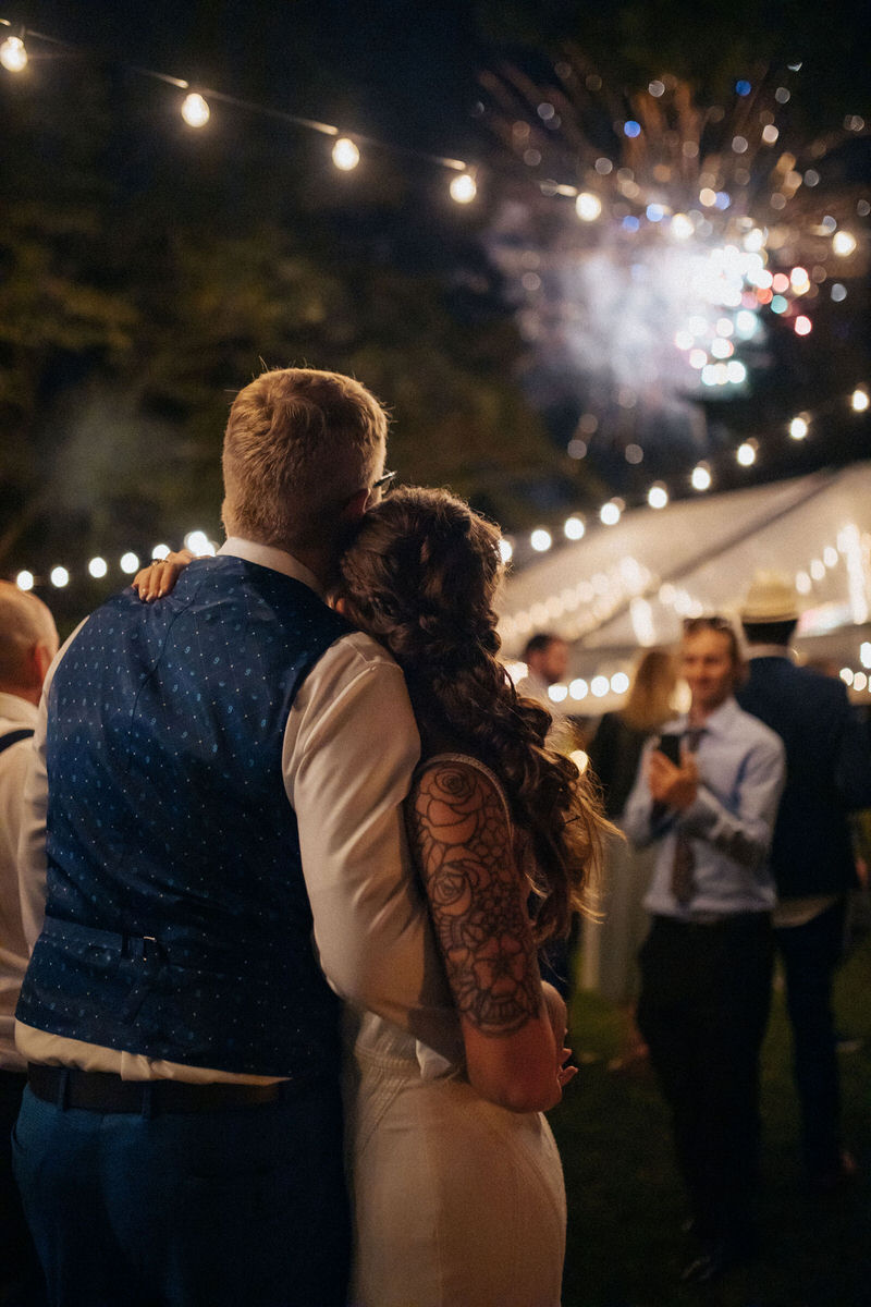 couple watching fireworks with wedding guests at an outdoor reception 