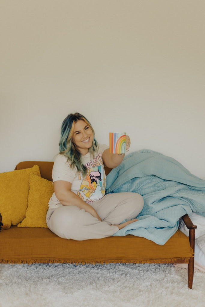 person sitting on a couch holding a rainbow coffee mug