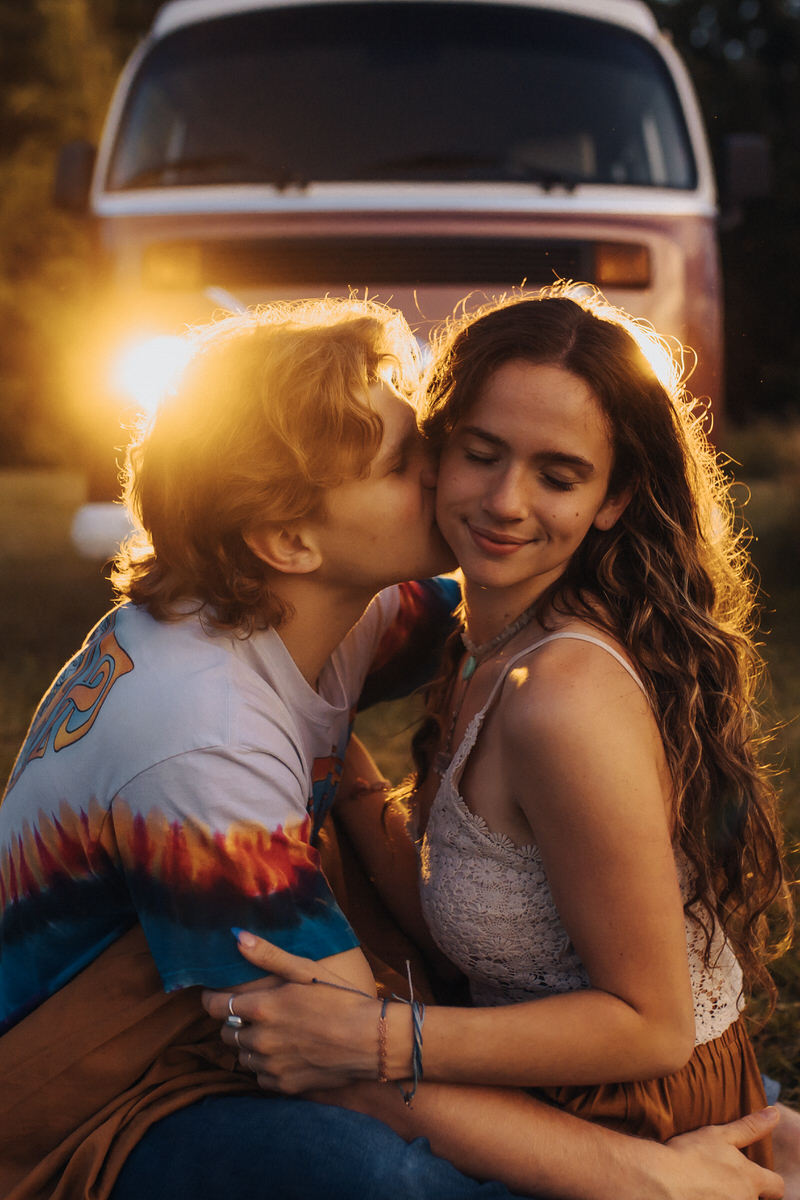 couple sitting in front of their car together while one kisses the others cheek
