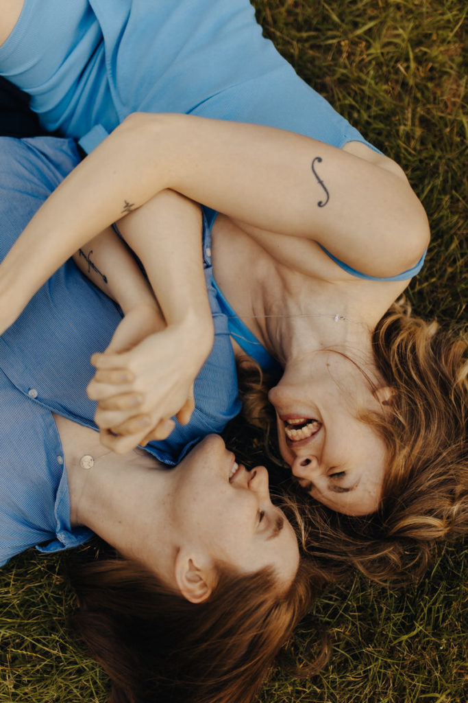 couple laying down on the grass looking at each other and holding hands