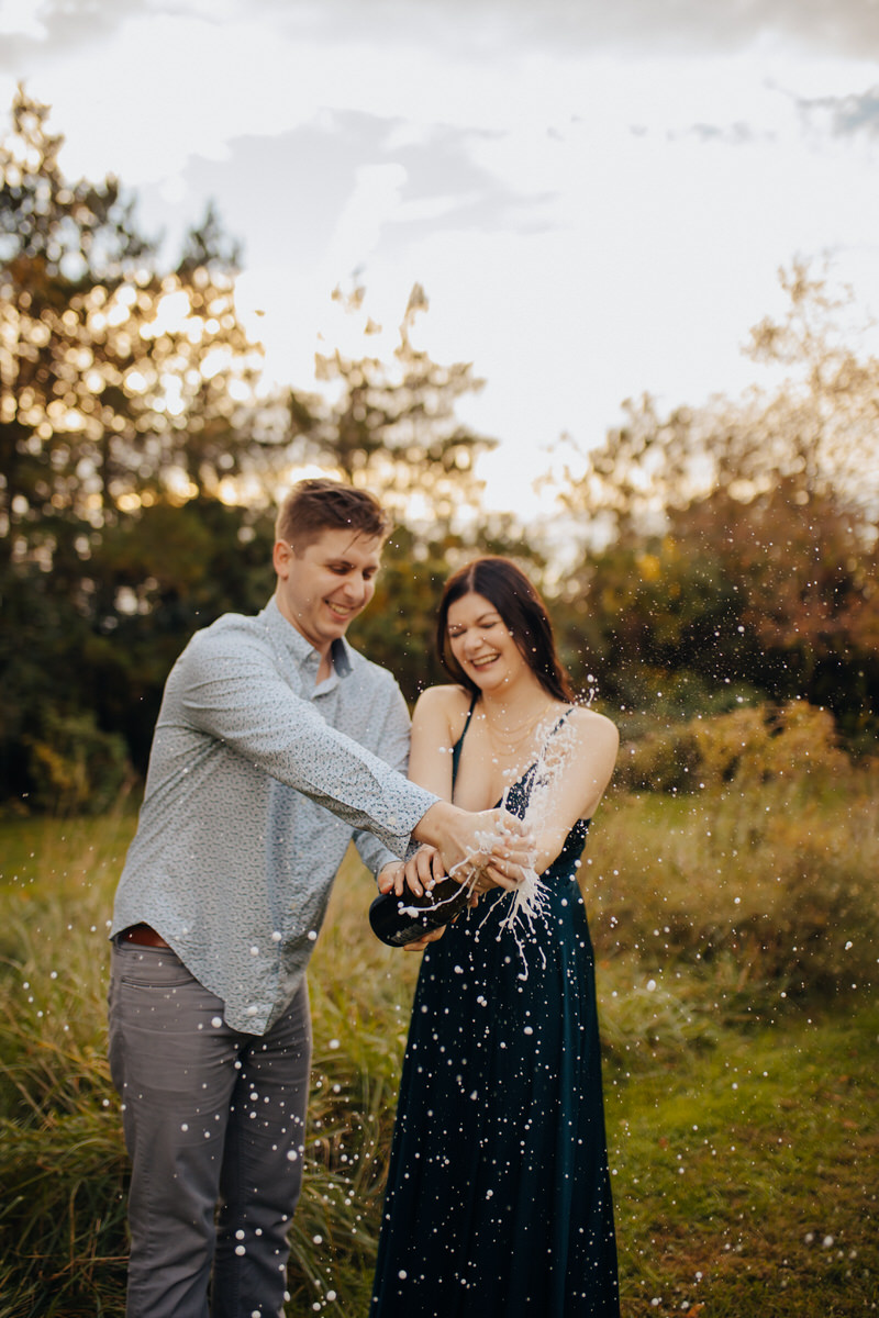 couple popping a bottle of champagne in a field