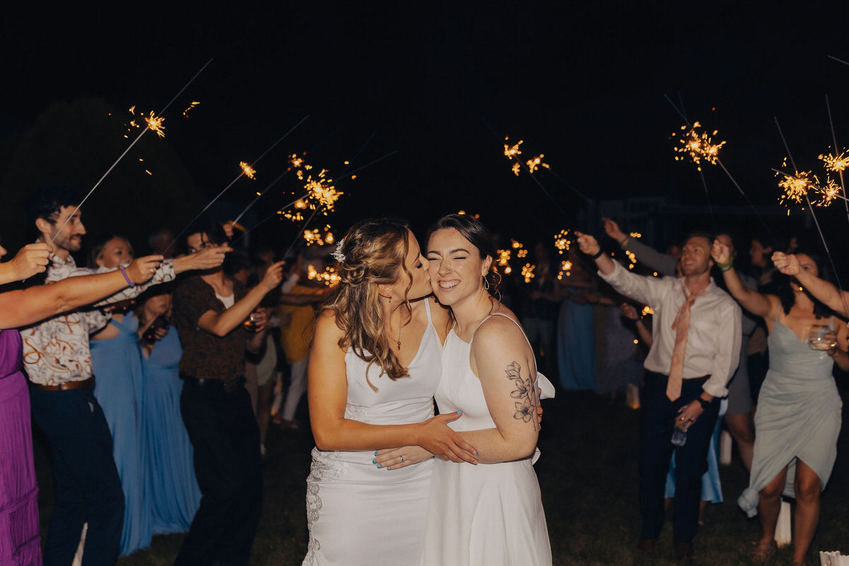 person kissing spouse on cheek while guests hold sparklers up