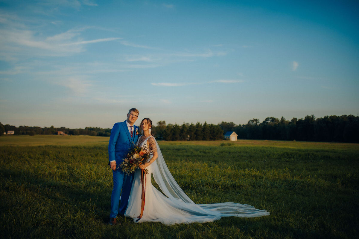 wedding couple standing together in a large field at dusk