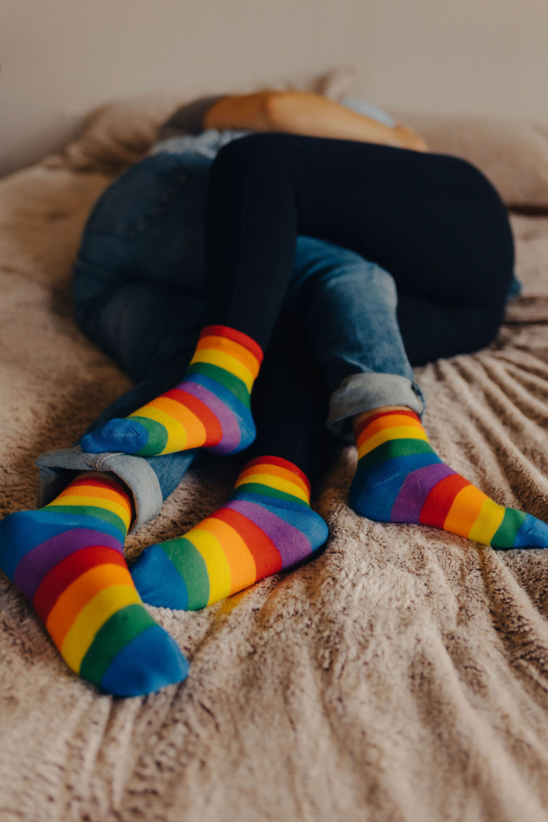 couple with rainbow socks laying on a bed together 