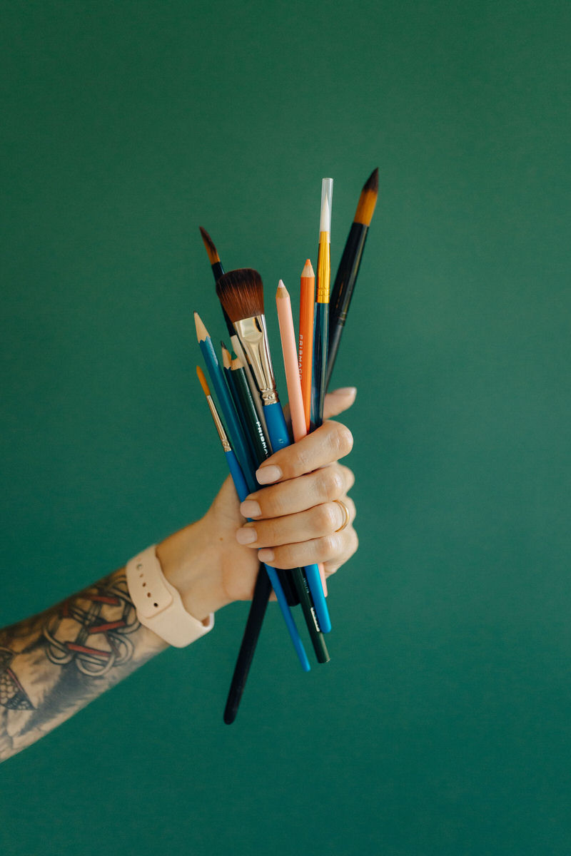 tattooed arm holding a handful of paintbrushes and colored pencils 