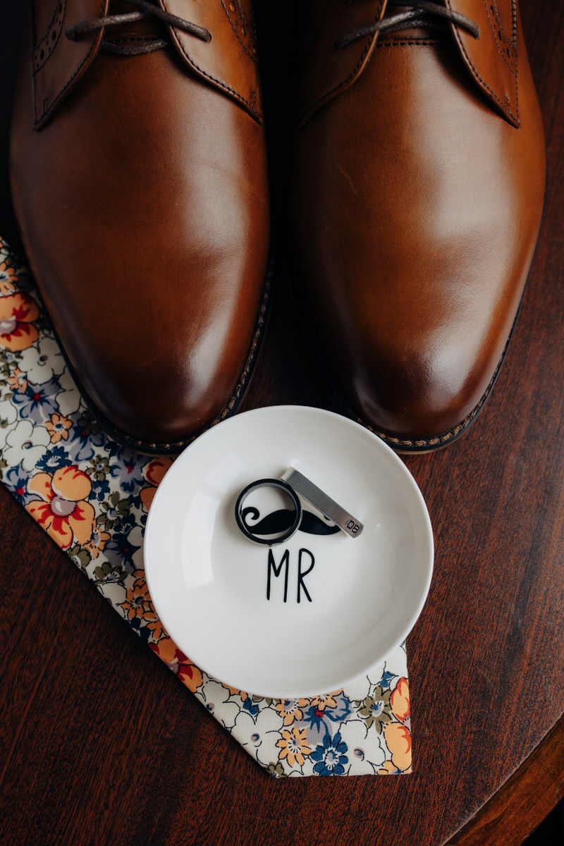 ring in a small dish with the word mr on it on a table with a tie and brown shoes