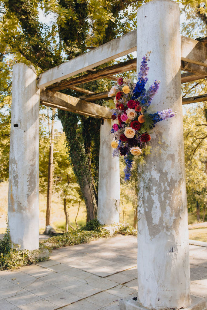 large white washed pillars connected by beams at the top with a bouquet of flowers hanging from one pillar