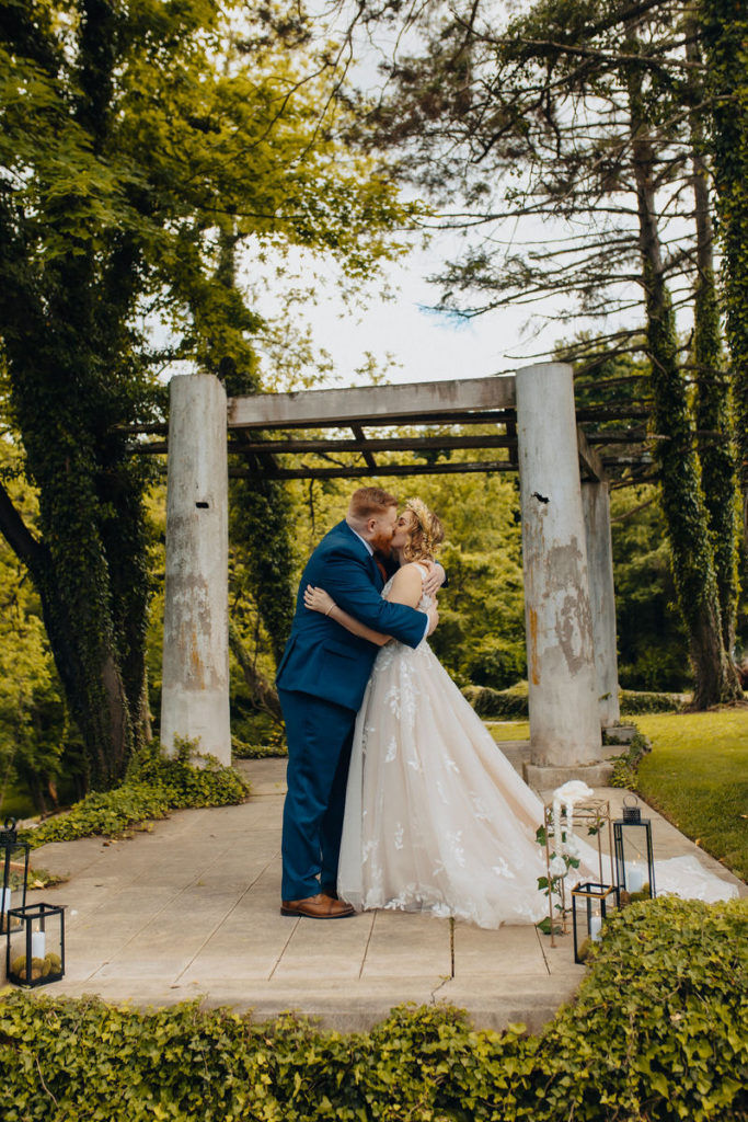 wedding couple kissing in front of large wood pillars in a wooded area