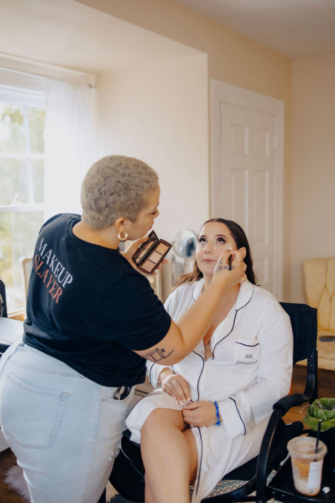 make up artist applying to make up to a person's face who is sitting in a chair 