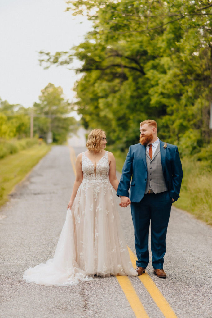 wedding couple holding hands and standing in the middle of a road surrounded by trees