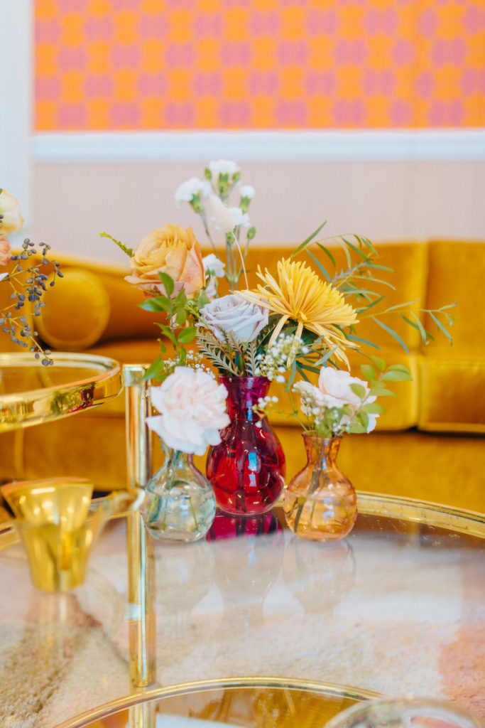 colorful vases of flowers sitting on a clear table with a yellow couch behind