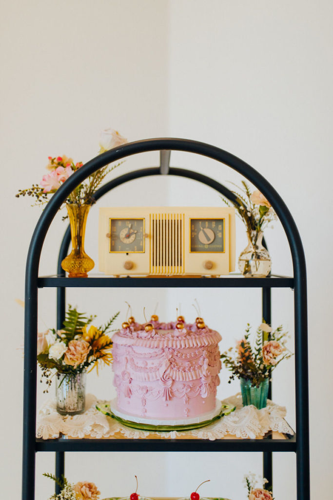 black arched shaped shelf with flowers, a wedding cake, and a radio on it