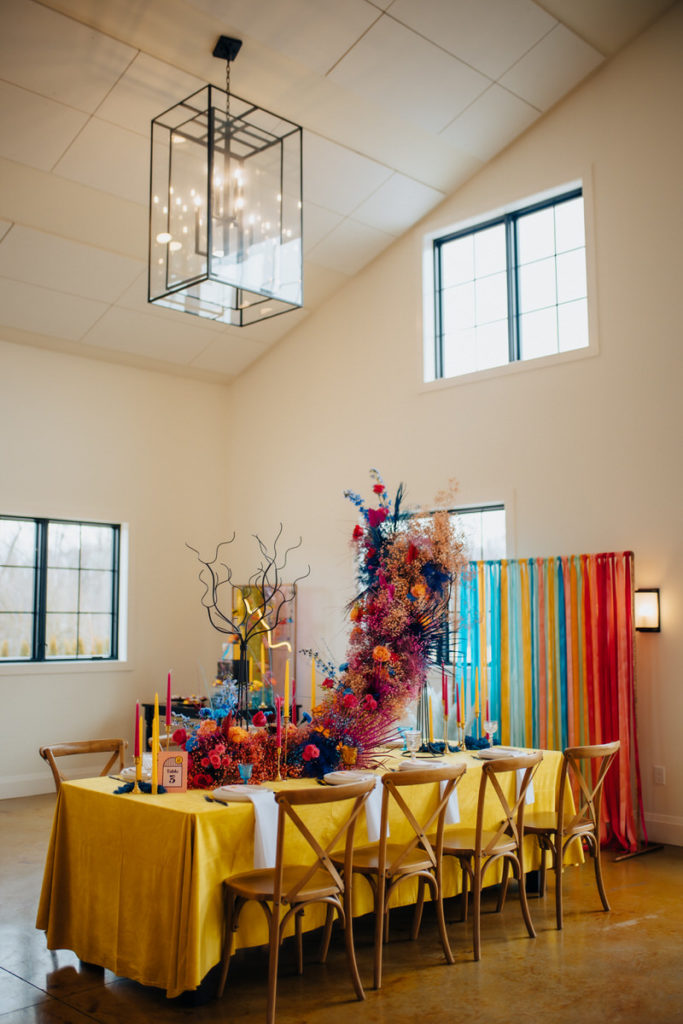 long table with a yellow table cloth and a large, colorful flower arrangement in the middle 