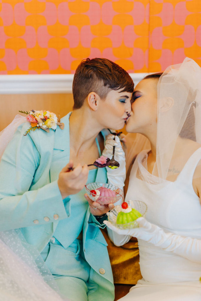 wedding couple kissing while they both hold desserts 