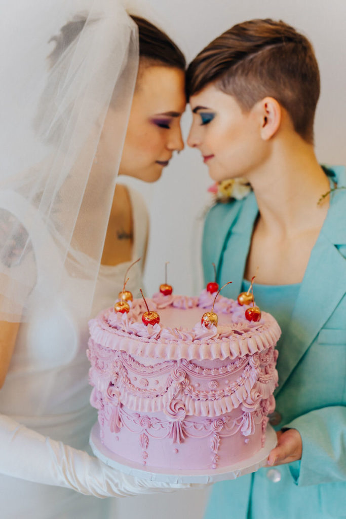 wedding couple standing forehead to forehead while holding a pink cake 