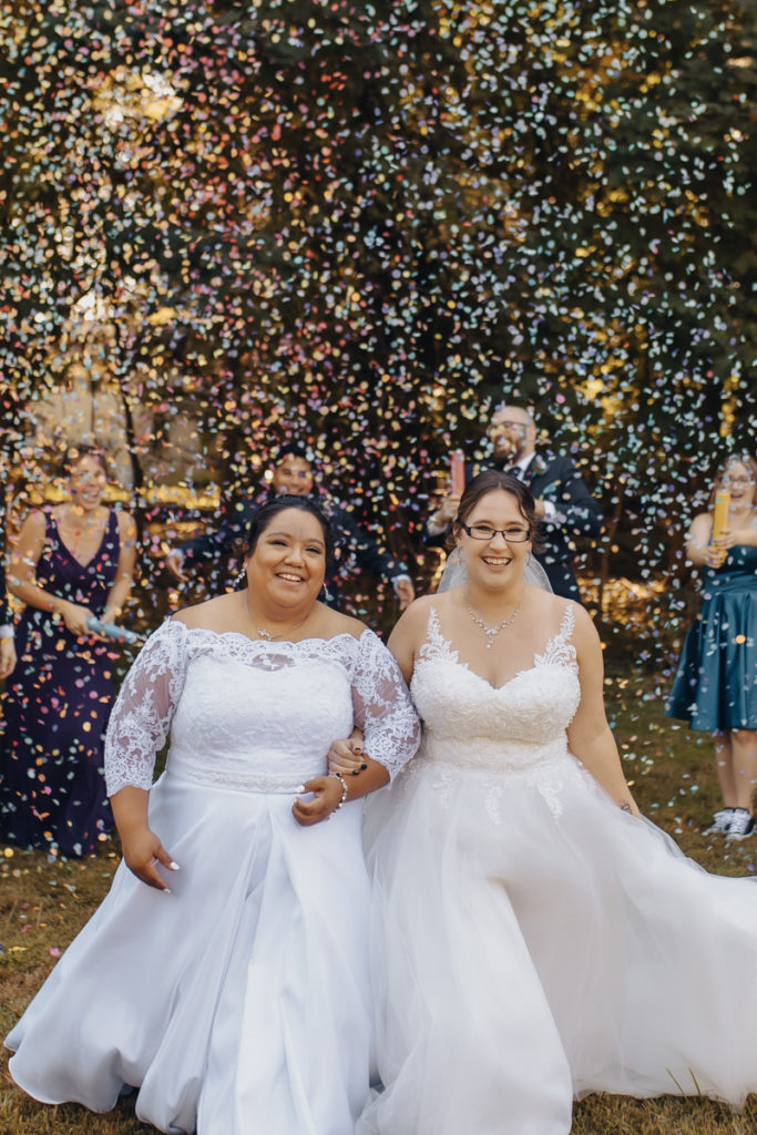wedding couple walking together holding hands while guests throw confetti around them