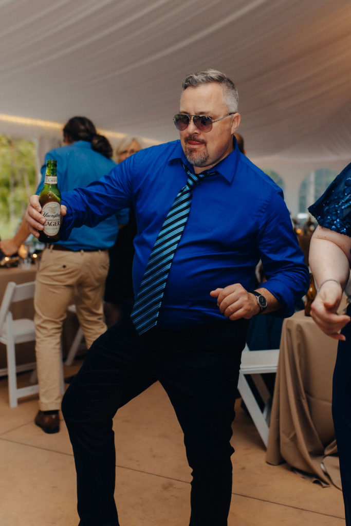older man in sunglasses holding a bottle and dancing