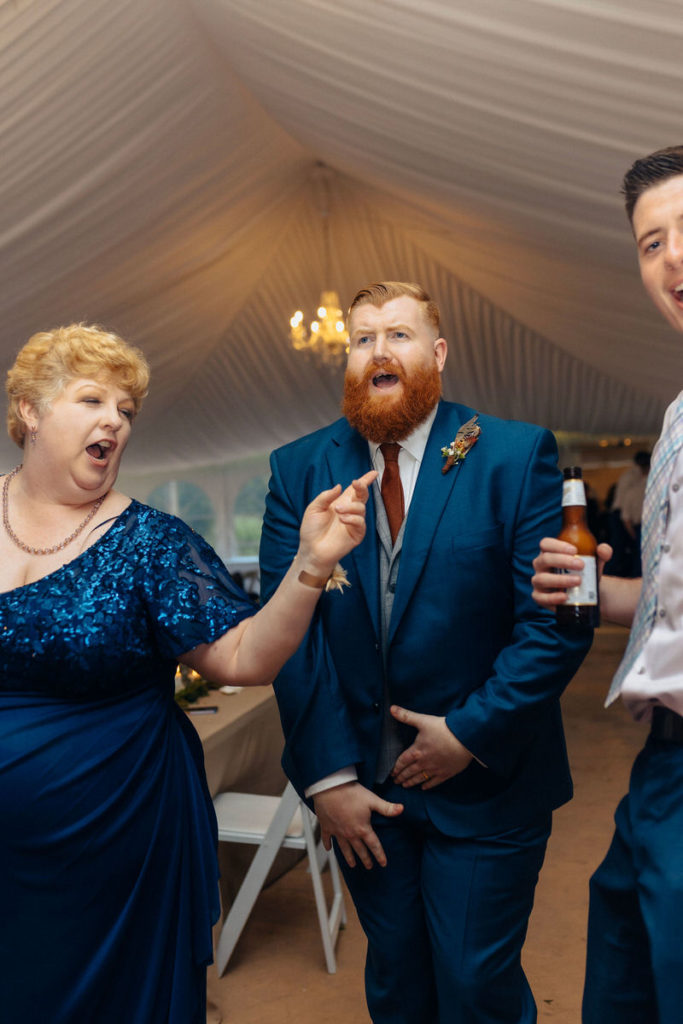 three wedding guests on the dance floor together while one of them holds a bottle 