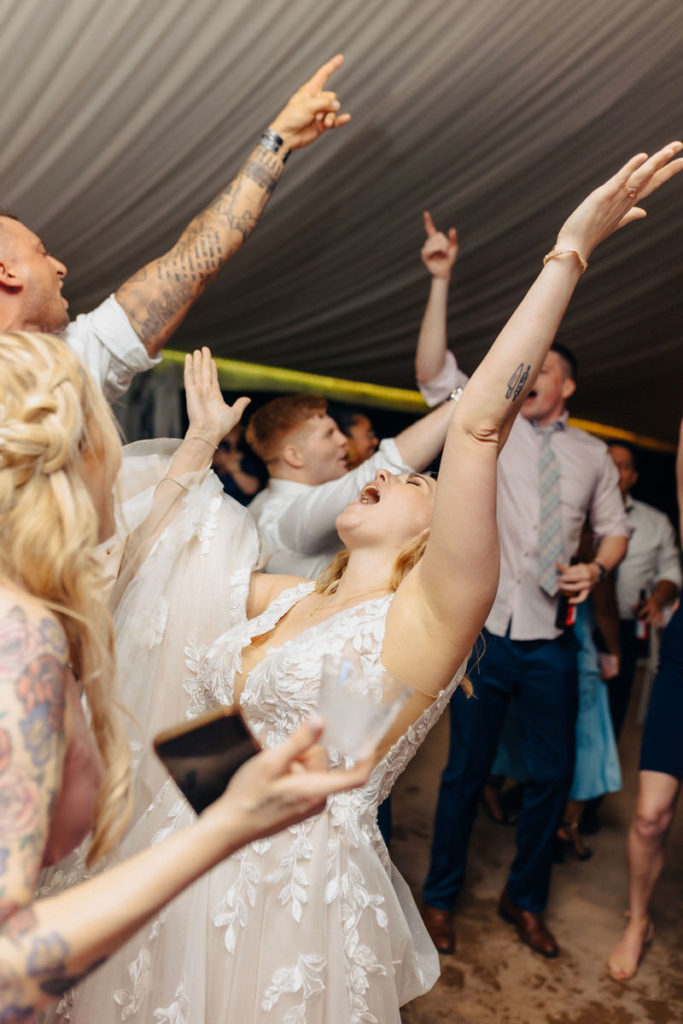 large group of wedding guests with their hands up singing and dancing 
