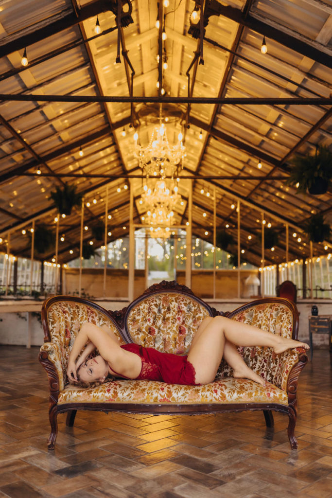 person in red lingerie lying on a vintage couch in a large barn 