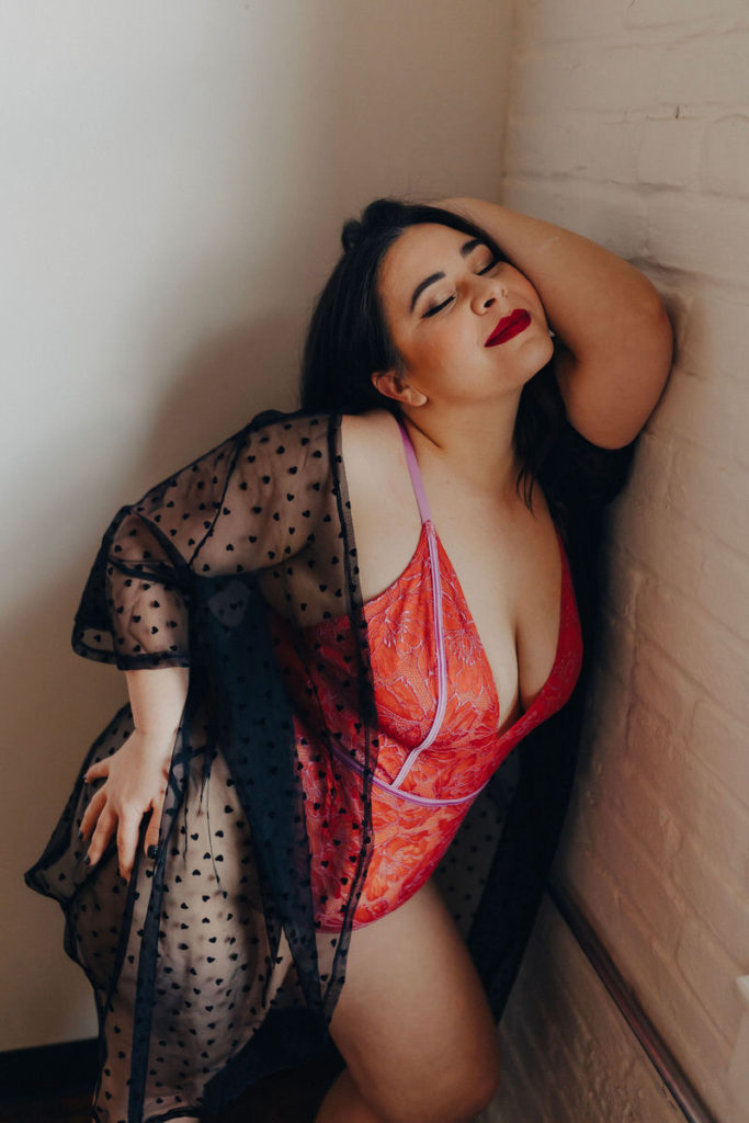 person in lingerie leaning up against a wall with one arm raised up to their face 