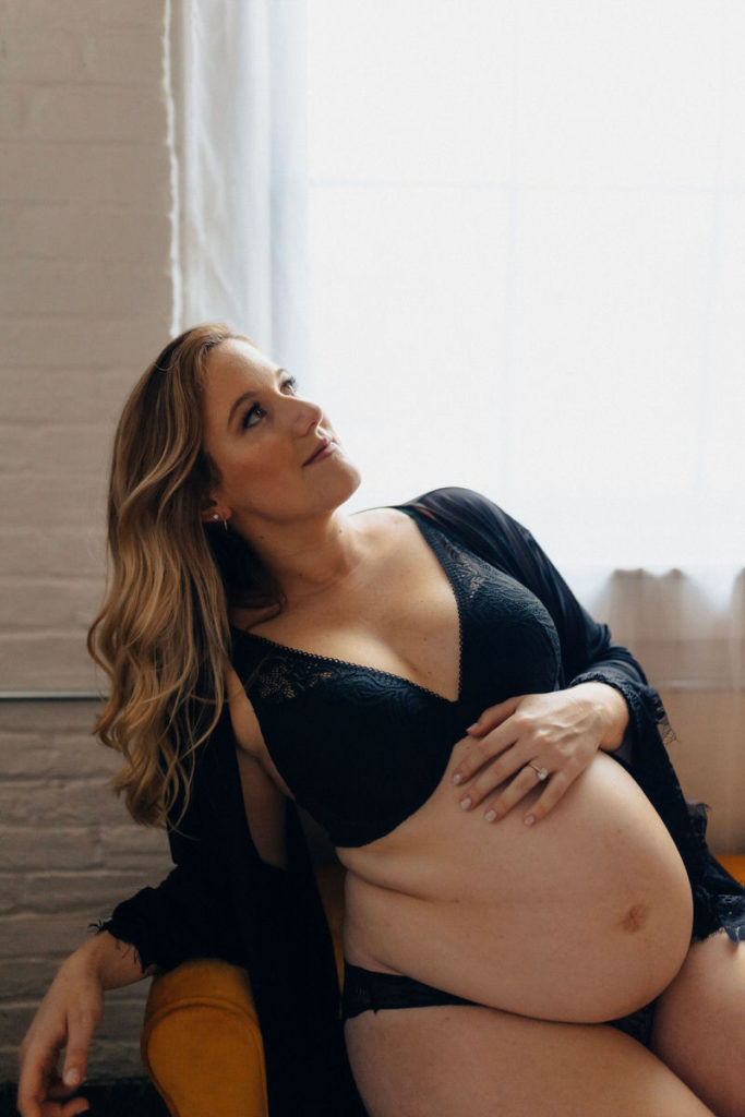 pregnant person in black lingerie leaning back in a chair and looking up 