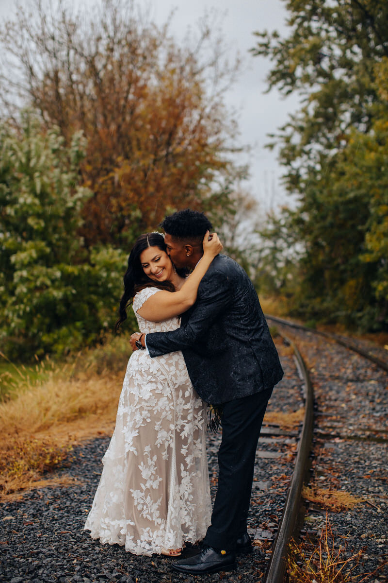 featured image for what to do with wedding photos featuring a wedding couple standing in a wooded area hugging as one kisses the other's cheek
