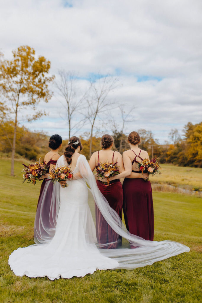 wedding party standing outside facing away from the camera with their arms around each other as they all hold colorful bouquets of flowers 