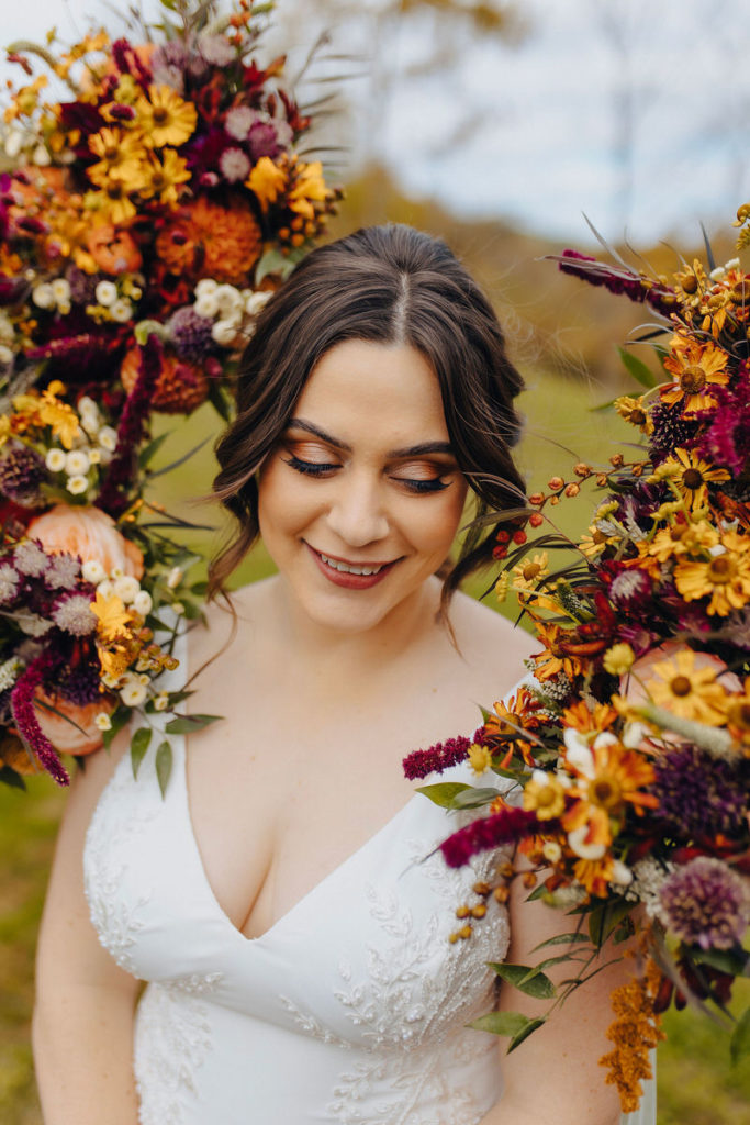 person in a white wedding dress looking down as they are surrounded with colorful bouquets of flowers on either side of their head 
