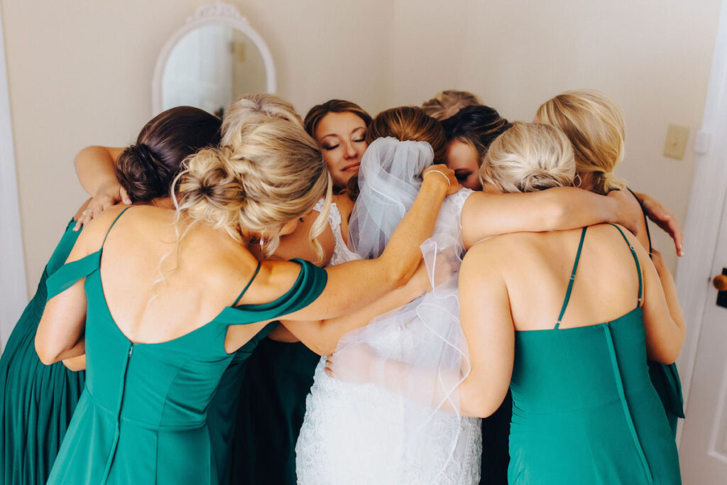 A bride and wedding party in a circle hugging each other. 