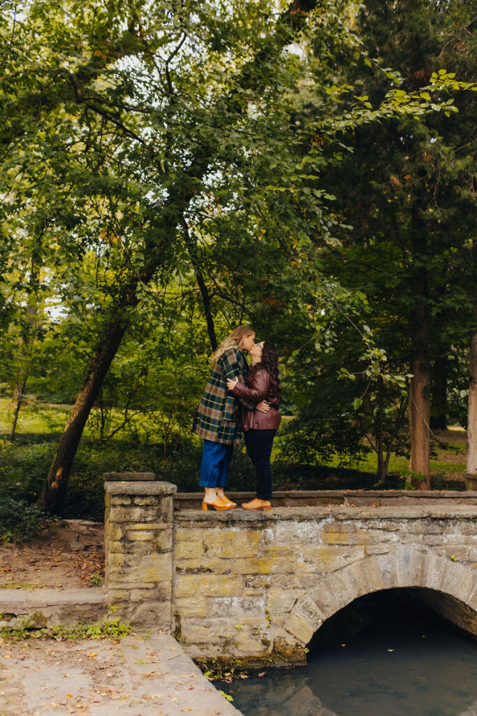 A couple standing on a small bridge kissing. 
