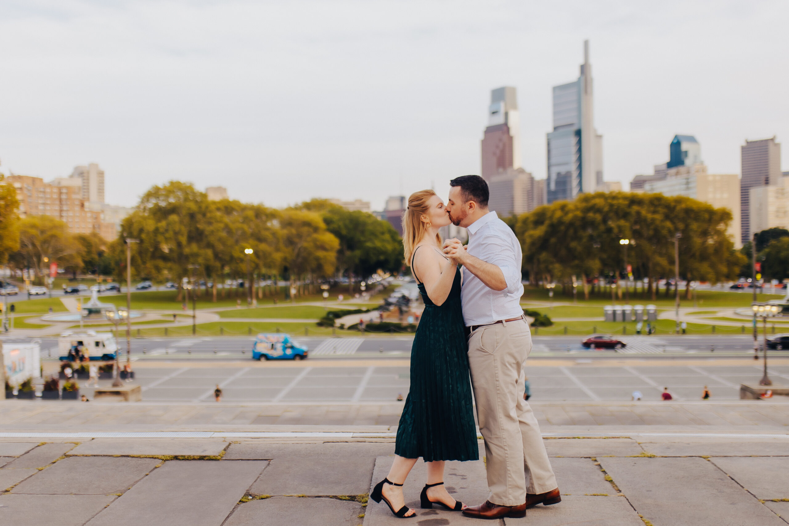 A couple kissing while standing at the top of a plaza staircase overlooking a city during engagement photos in Philadelphia