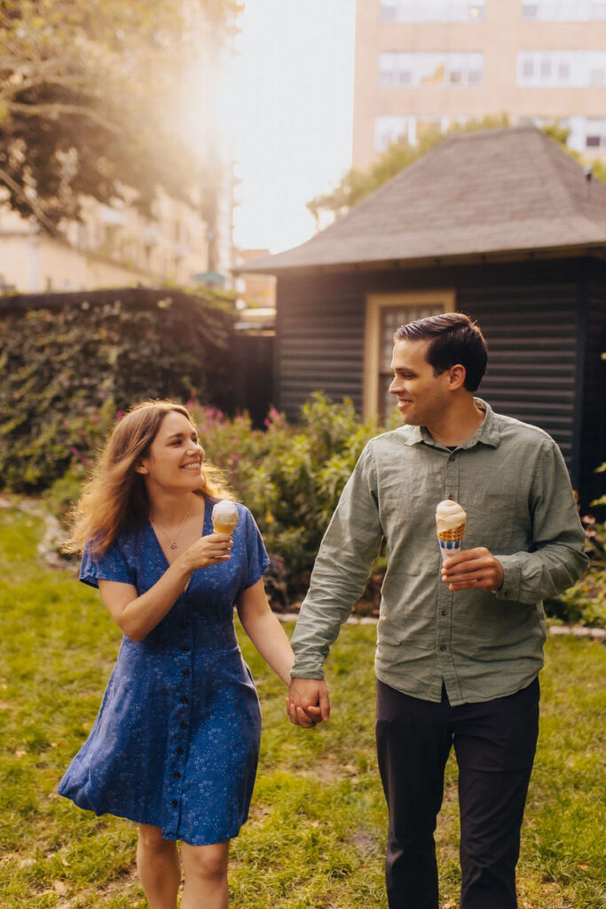 A couple walking together holding hands while eating ice cream. 