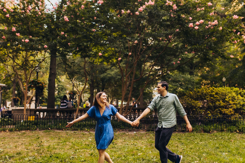 A couple holding hands and running through a park. 