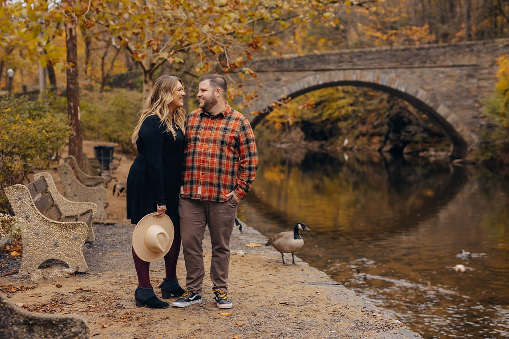 A couple smiling while they stand next to a river. 