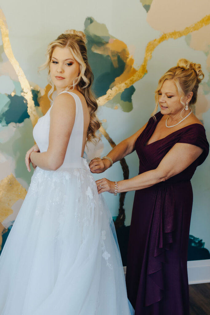 A woman helping a bride zip up their dress.