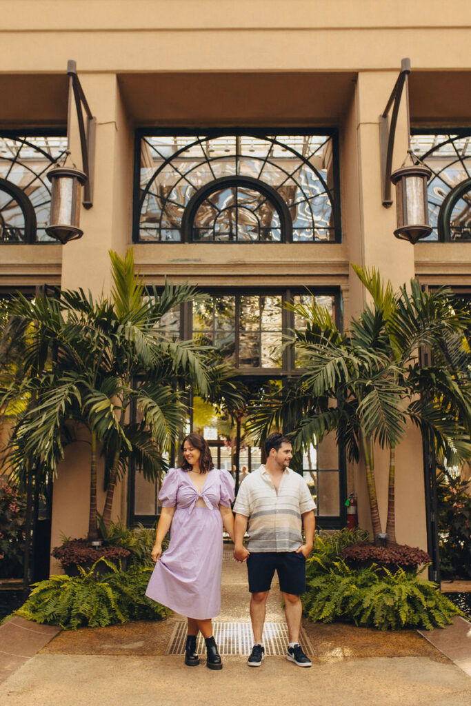 A couple holding hands while standing in front of a large conservatory.