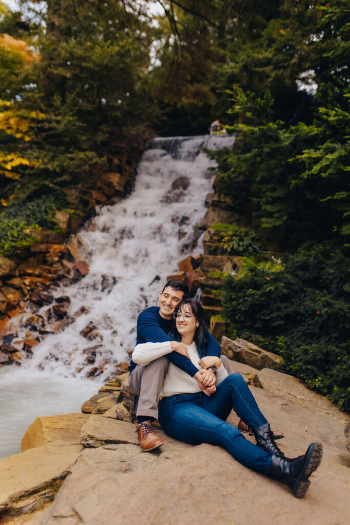 A couple sitting on a rock in front of a small waterfall.