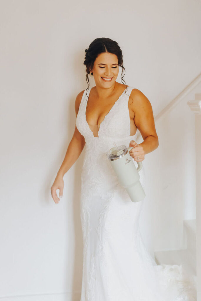 A person walking down the stairs in a wedding dress holding a large cup. 