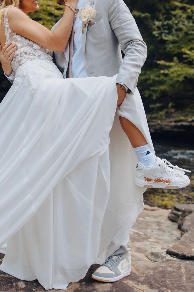 Newlyweds in a playful pose, with one lifting their dress to reveal sneakers.